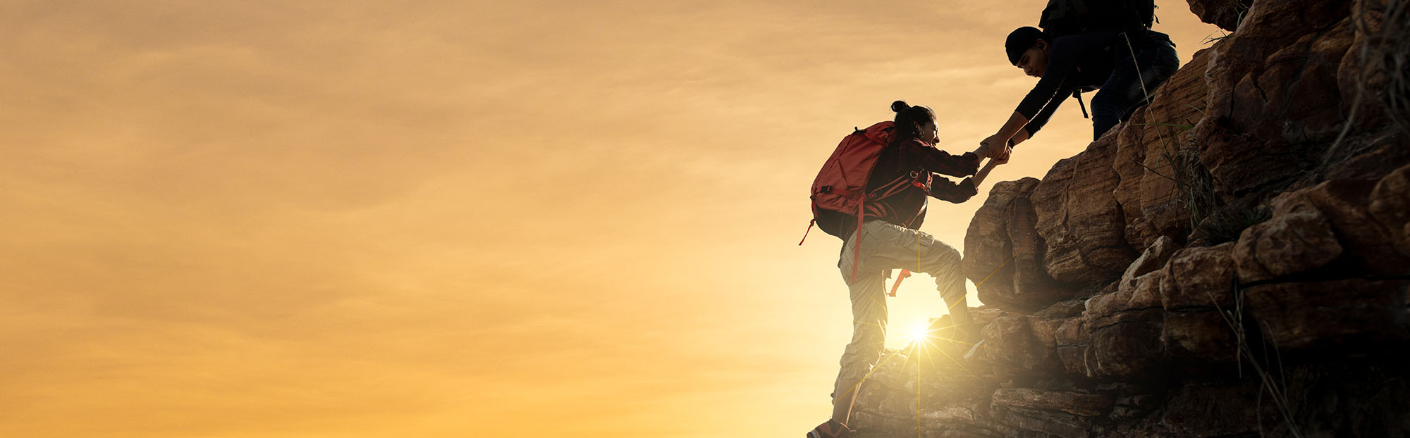 Ein Paar hilft sich gegenseitig beim Wandern in den Bergen. Silhouette mit Sonnenlicht.